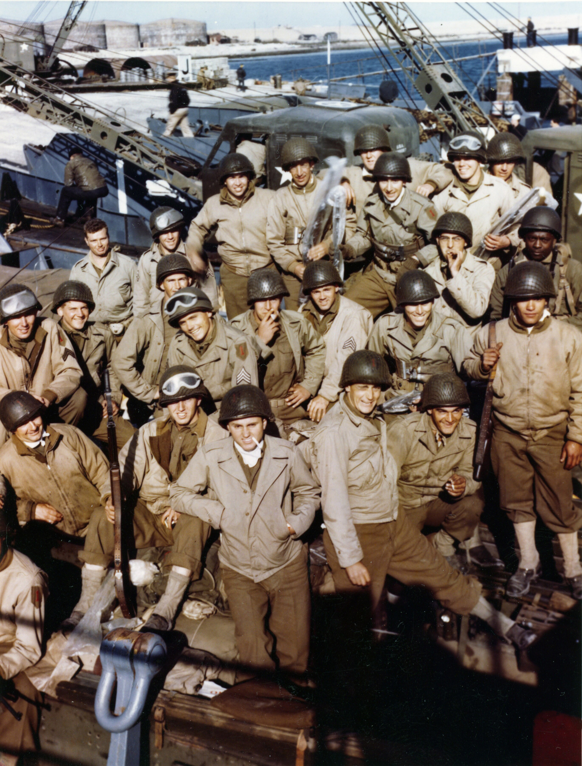 1st Infantry Division soldiers, some with their rifles already wrapped in waterproofing cellophane, pose for a photo aboard ship before leaving England for the D-Day invasion.